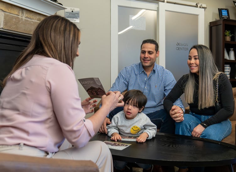 A Betenbough Homes team member meets with a young family and their child inside a New Home Center, discussing home options around a coffee table.