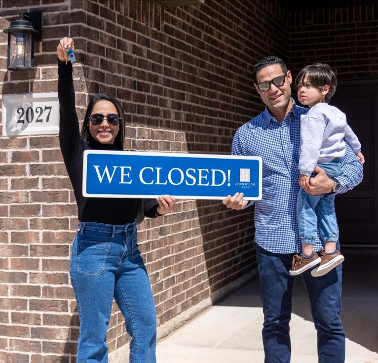 Photo of first-time home buyers holding the keys to their new Betenbough home and a sign that says "We Closed!"