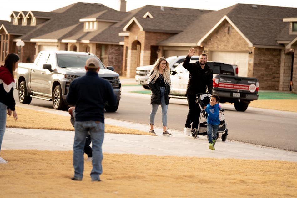 A family in a Betenbough community wave to their neighbors as they take a walk.
