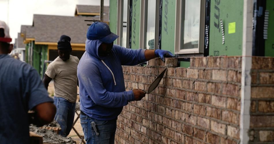 Photo of a trade partner laying energy-efficient exterior brick around energy-efficient double-paned windows on a new Betenbough home.