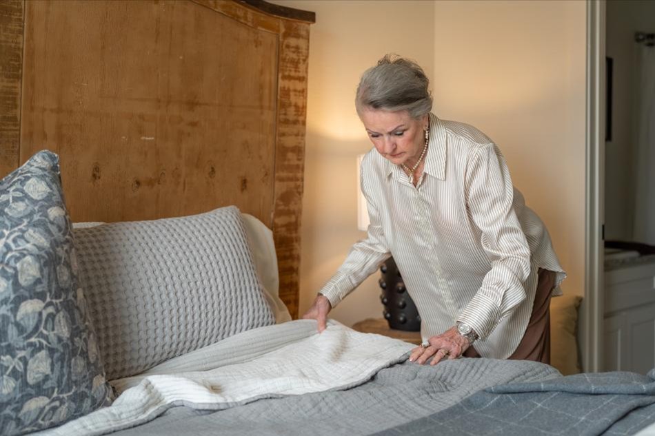 Photo of a retired woman making the bed in her downsized Betenbough home.