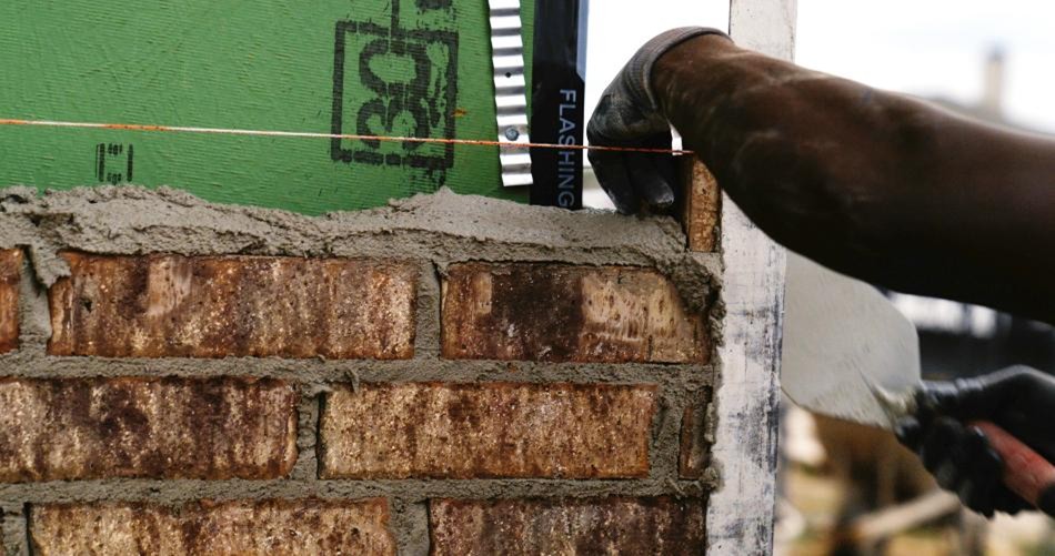 Photo of a brick-layer laying energy efficient brick on the exterior of a Betenbough Home.